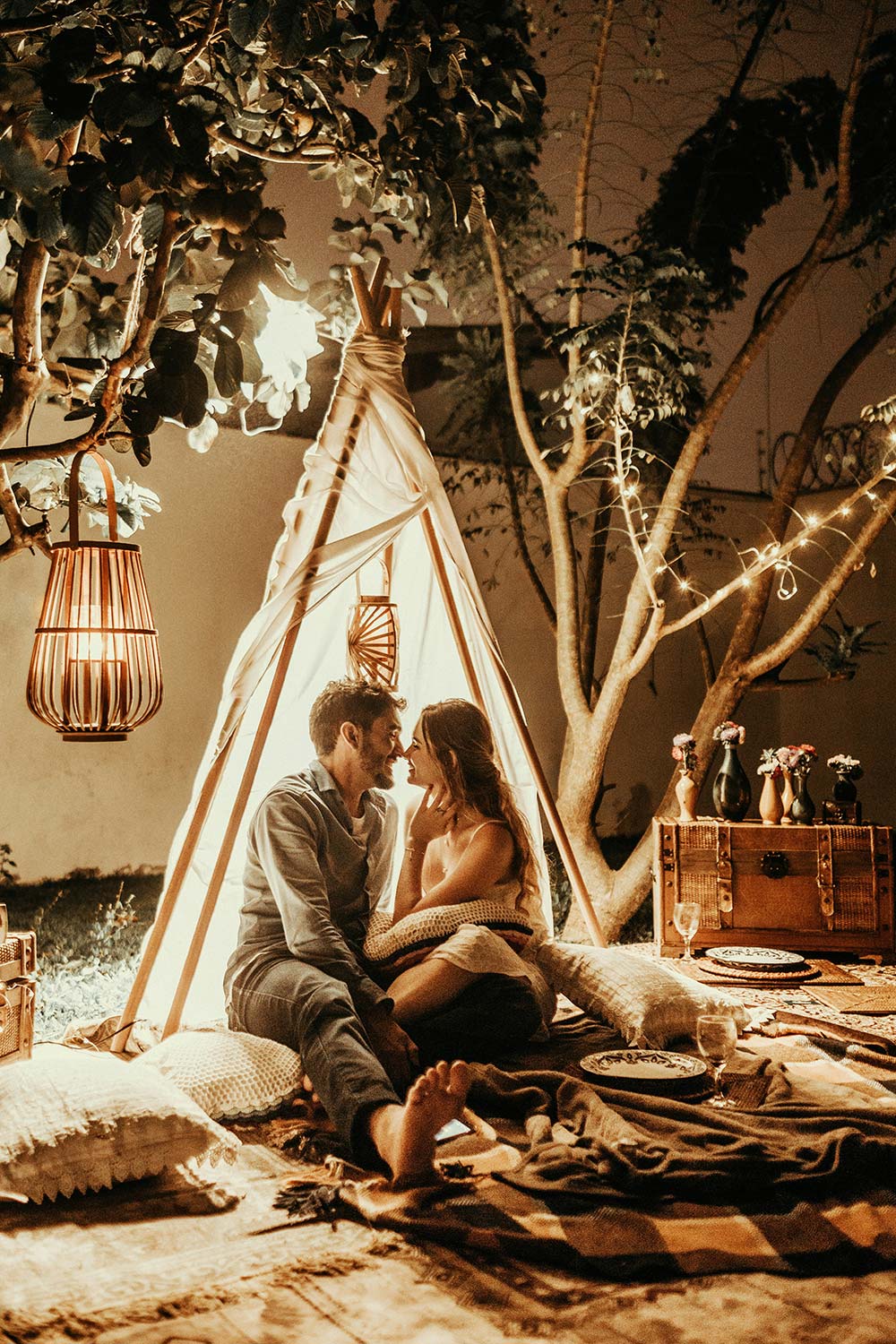 A couple shares a cozy, candlelit moment inside a small tent at night.