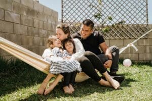 A family of four relaxes together in a hammock in a sunny backyard.