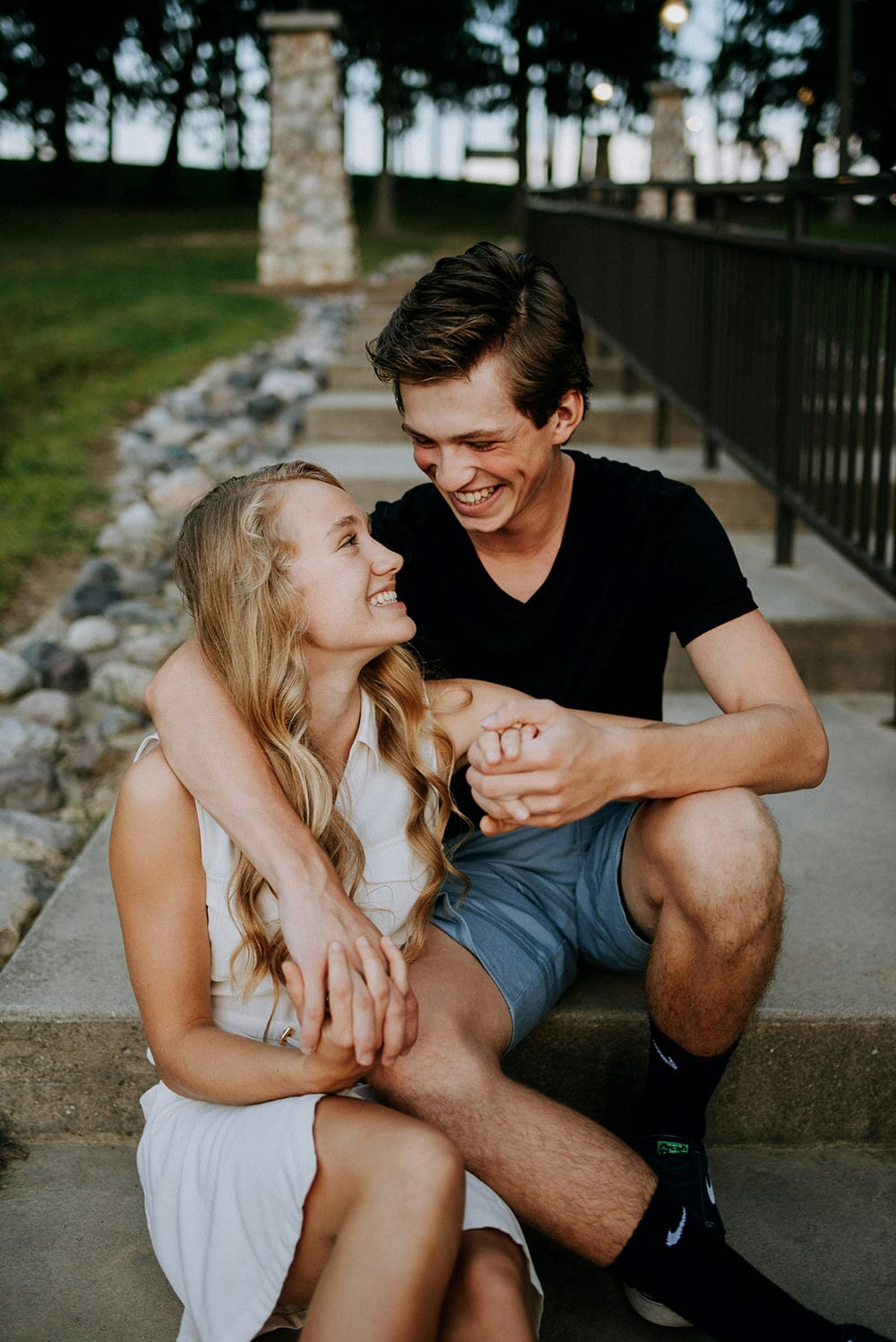 A laughing young couple sits on outdoor concrete steps.