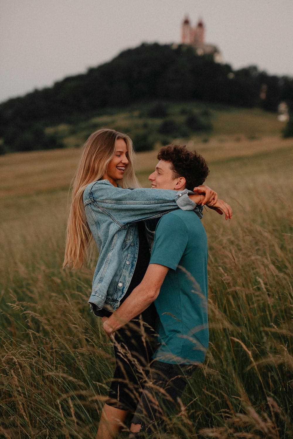 A man lifts a laughing woman in a denim jacket