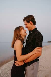 A smiling young couple embraces on a sandy beach at sunset