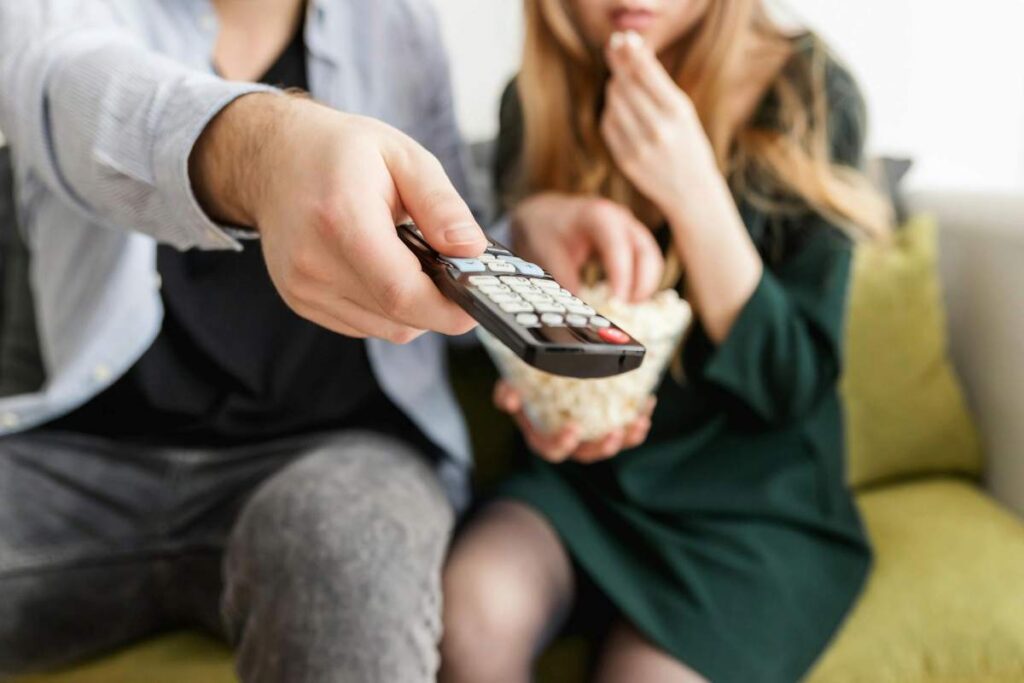 Couple sitting on a couch watching TV together with popcorn, reflecting small relationship moments.