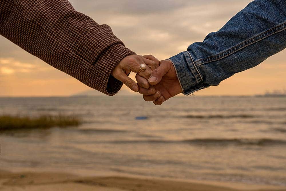 close-up of a couple holding hands on a beach.