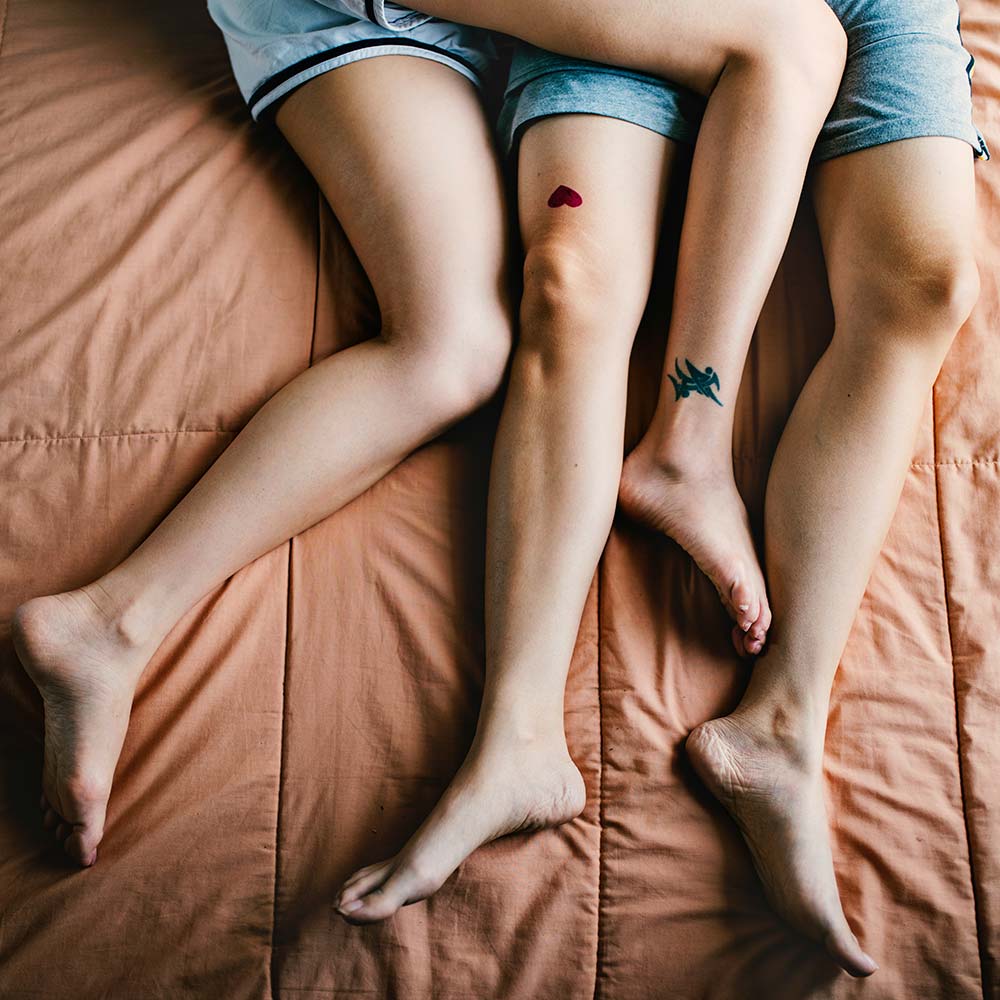 close-up of legs lying on a bed with tattoos.