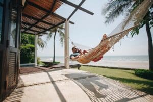 couple relaxing in a hammock on a beach patio under palm trees.