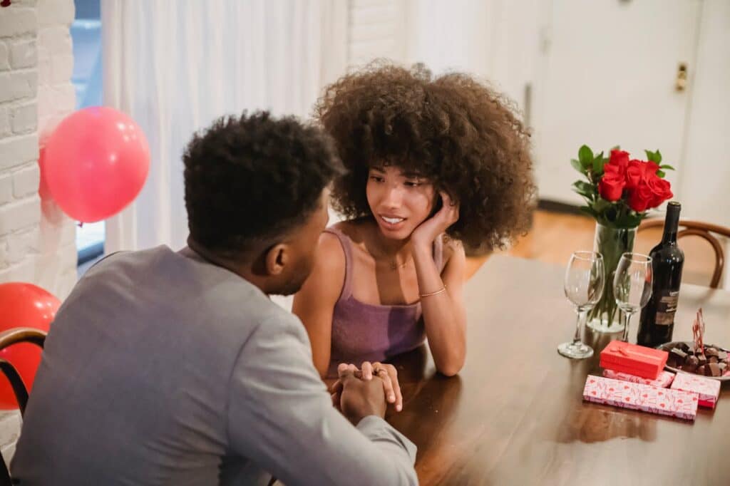 Couple having a heartfelt conversation during a romantic dinner at home with gifts and red roses on the table.