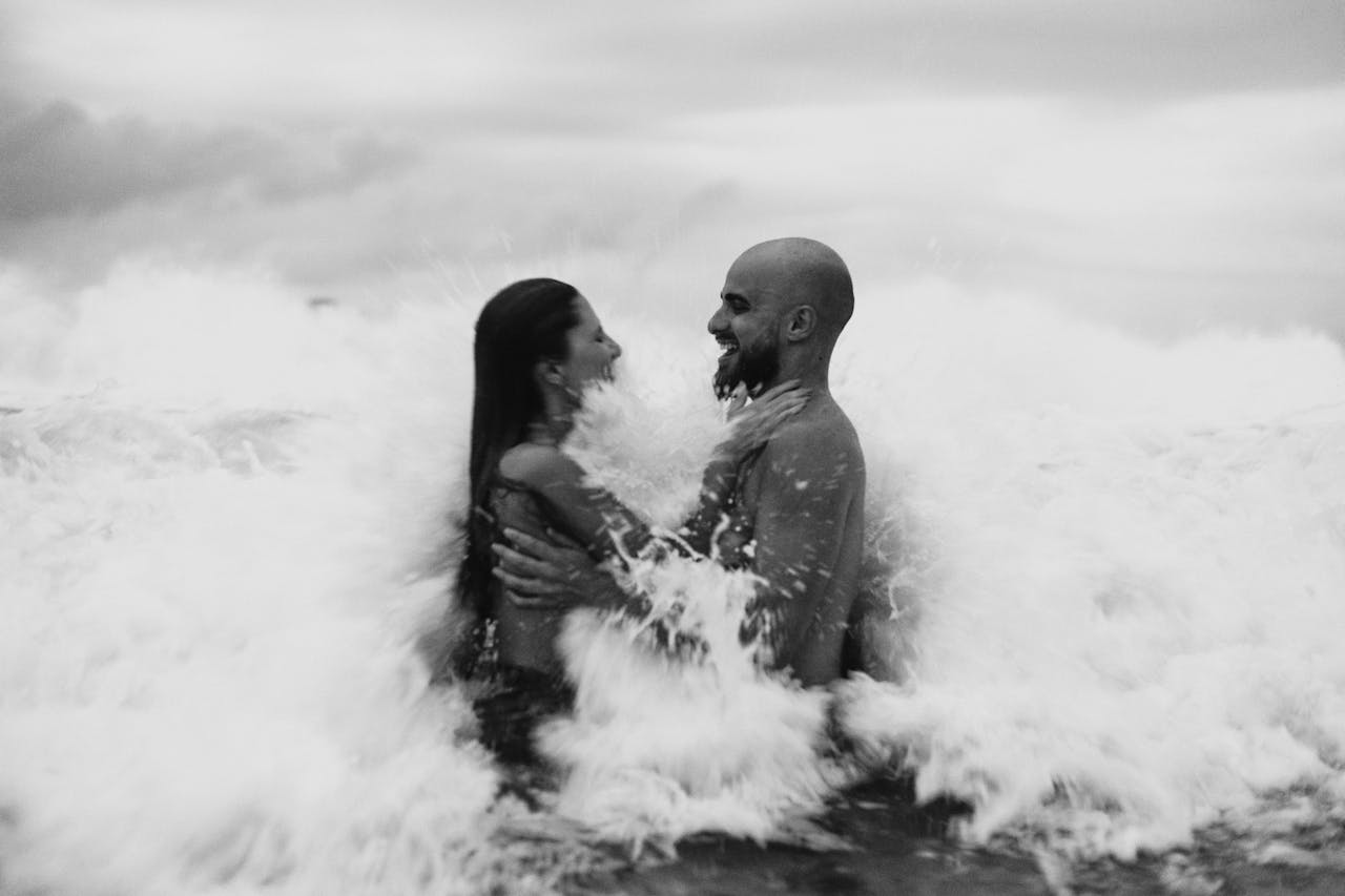 Couple embracing and laughing as ocean waves splash around them, symbolizing renewed passion and connection