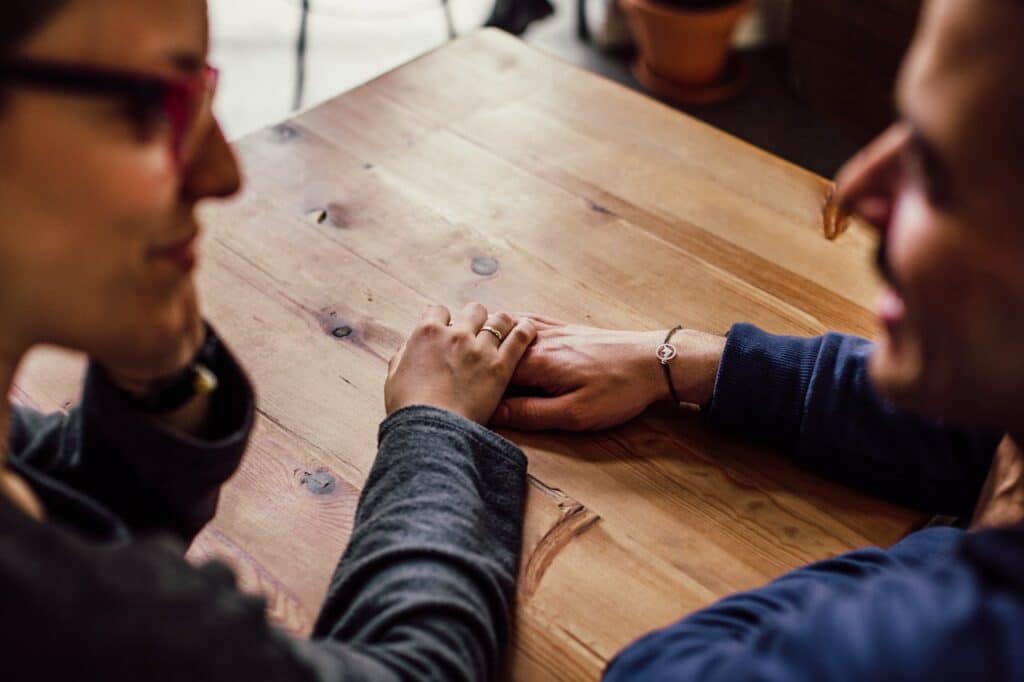 Couple holding hands across a wooden table during a heartfelt conversation, symbolizing emotional connection and understanding in relationships.