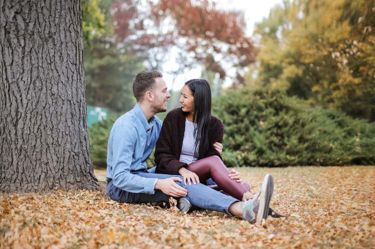 Couple sitting under a tree in a park, smiling and talking openly, representing healthy communication and closeness in relationships.