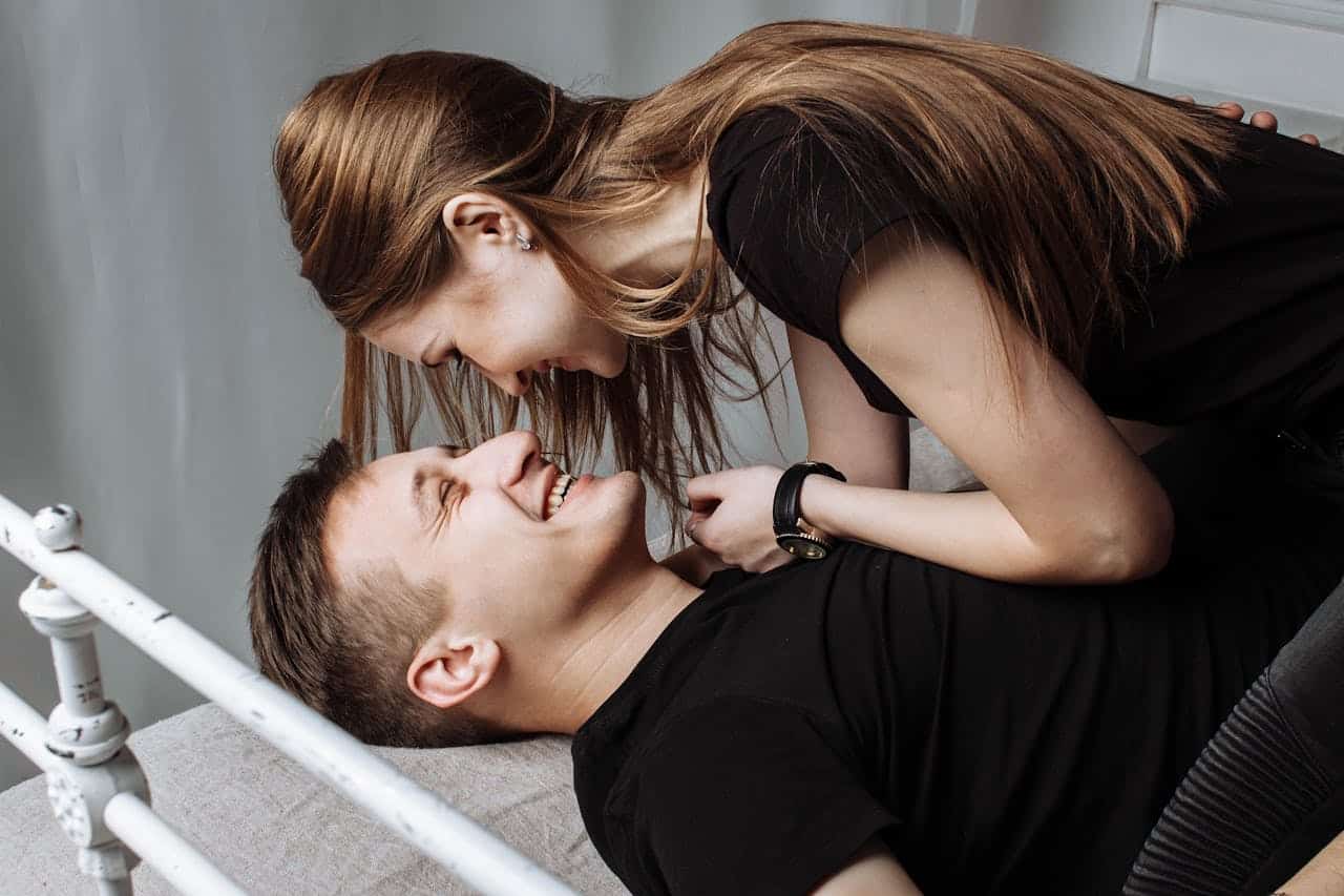 A couple laughing and sharing a close, intimate moment on a bed, representing emotional connection in attachment-based sex therapy.