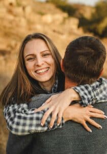 smiling woman in a plaid shirt hugging a man from behind.